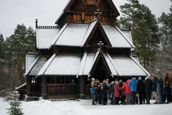 En gruppe mennesker står samlet utenfor stavkirken på Norsk Folkemuseum. 