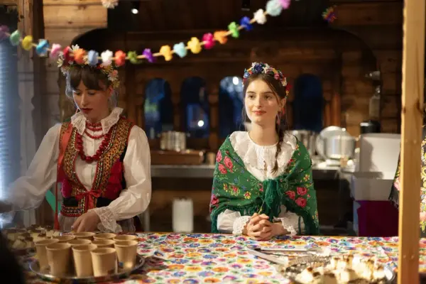 To kvinner iført tradisjonelle klær fra Polen deler ut mat og drikke. Polsk julepynt henger i taket.  