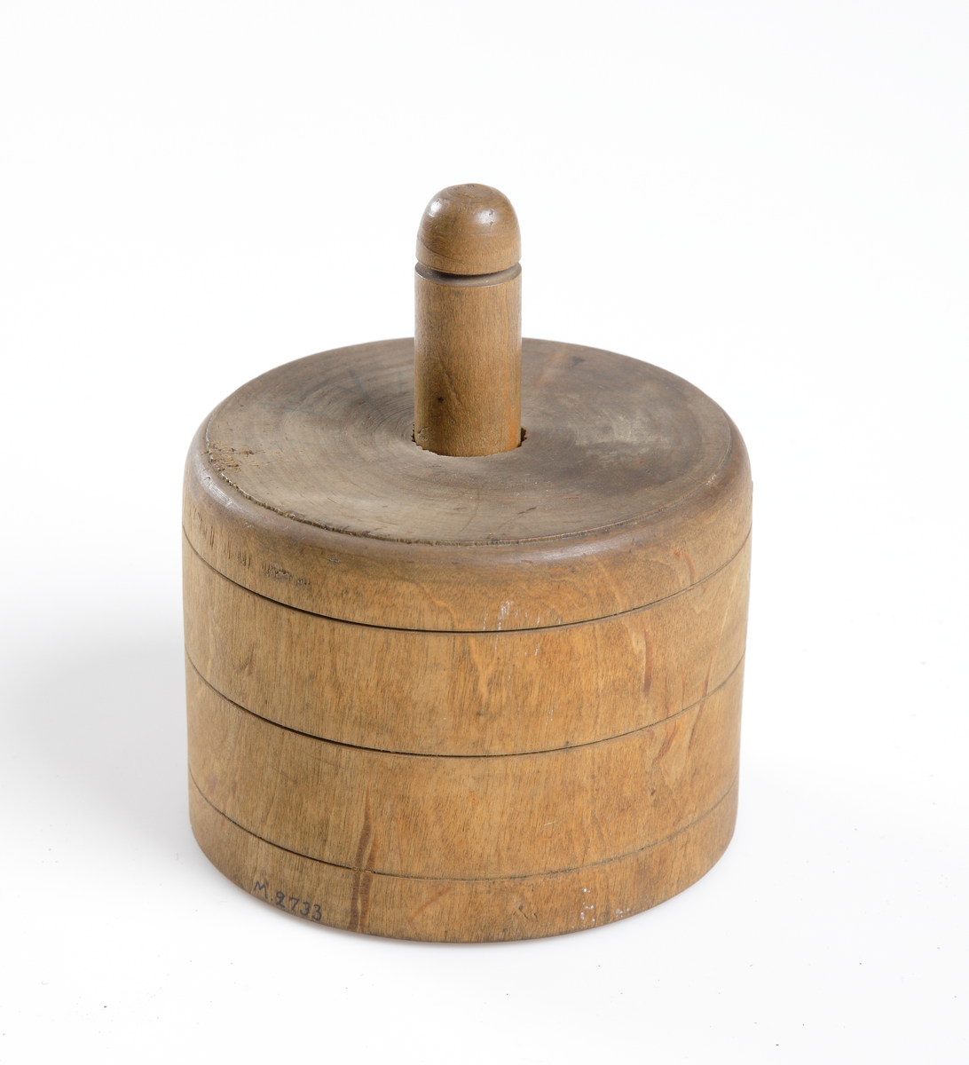 Smörpress av trä med lock. Cylindrisk. Skuren dekor i lockets undersida.
Inskrivet i huvudkatalog 1904.