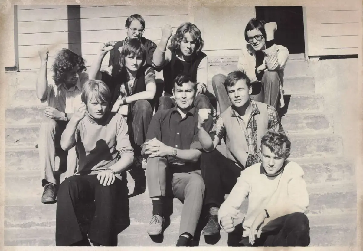 Ei gruppe demonstrantar sit med kvar sin arm lyfta og knytt neve, ute på ei betongtrapp