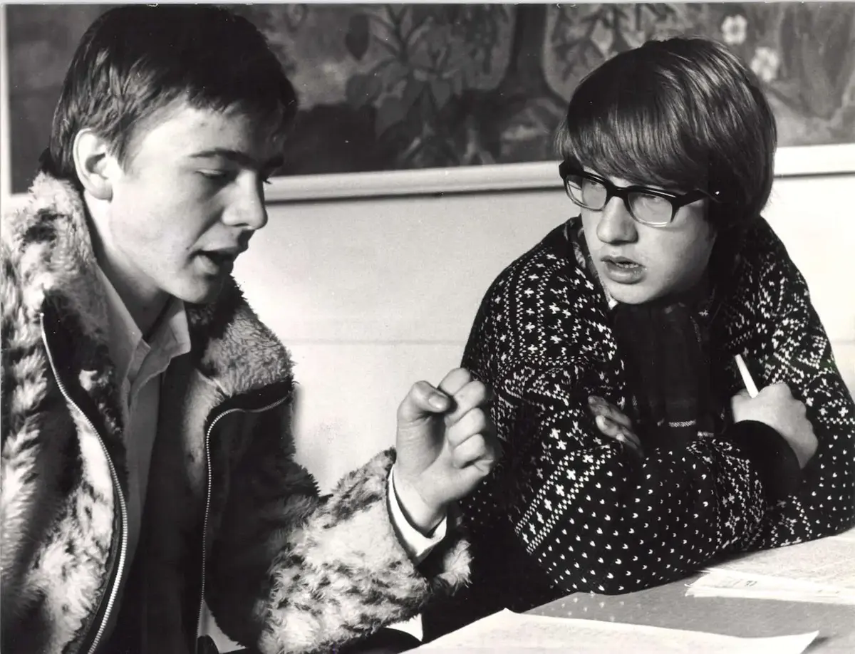 Svart kvitt bilde av to elevar ved Øystese realskule og gymnas, Ottar Wiik (t.v.) og Knut O. Dahle, som sit ved eit bord og diskuterer.