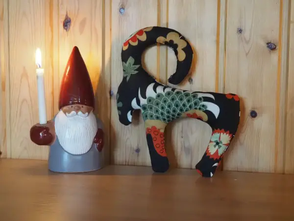 Mönstrad bock och tomte som håller ett ljus med träpanel i bakgrunden.