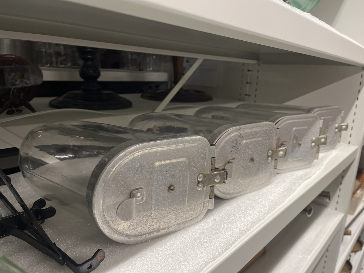 Ställ och glasbehållare för försäljning av karameller. 
a. Svart metallställning.
b-g. Glasbehållare med lock av aluninium. Locken öppnas genom att fällas ner. Text på några av locken "DIX Miniatyr AB JOHN FRÖBERG FINNSPÅNG".
h. Skopa av alumunium.

Från Arne Ekströms handelsmuseum.