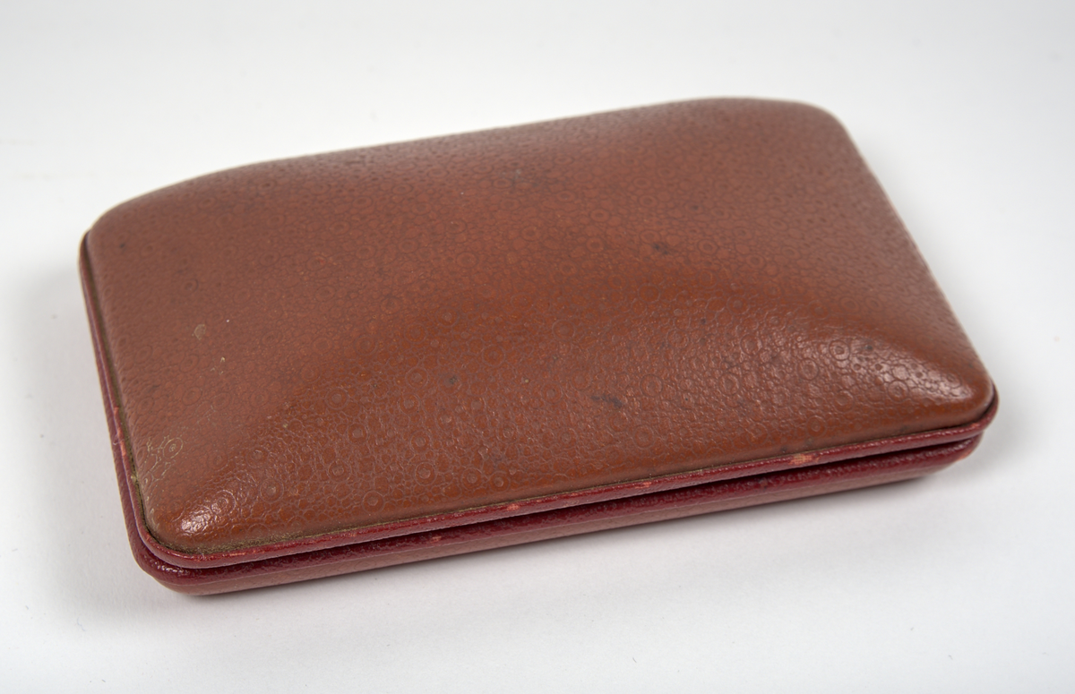 Armbandsur med tillhörande etui.

a) Damarmbandsur i art deco-stil med rektangulärt boett och länk i vitmetall. Urtavla med avlångt kvadratisk form, med arabiska siffror och två visare. Länken består av dekorerade länkar med blomformade detaljer. Boettens baksida graverad “Edith 1931”. På insidan av länken graverat “Betty Lou”, samt stämplat “1/20 12K G.F.” och “E.B.R.”.

Stämpeln “12K G.F.” antyder att ytskiktet består av 12 karats (vitt) guld, så kallad gold filled-metall.

b) Etui med kvadratisk form och högt vält lock. Utsidan klädd i röd läderimitation av formpressad plast. Locket är på insidan fodrat med beige siden och bär texten: "An Illinois Watch as american as its name". Insidans nederdel klädd i beige filtmaterial med svart uppbyggnad av filt för fästning av armbandsuret. Undersidan bär fodraltillverkarens stämpel: *Oläsligt i kursiv stil* följt av "Patented boxes".