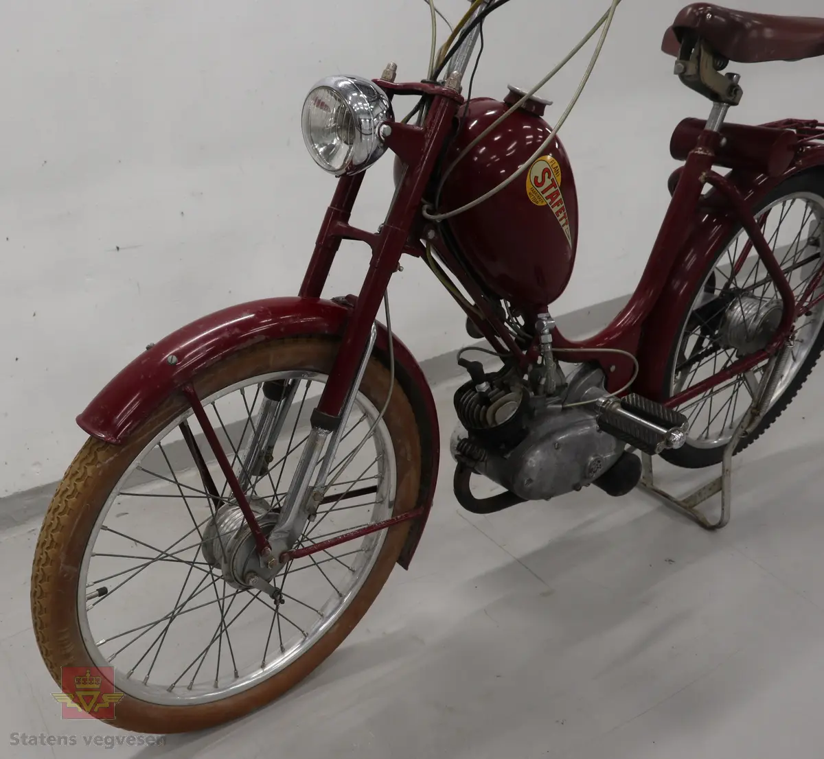 Flani Stafett type BFC-50. Mopeden er rød med svarte detaljer og flerfarget logo på begge sider av tanken. Merkeplate fra fabrikken sitter festet på gaffelen. Mopeden er utstyrt med en ensylindret BFC totakt forbrenningsmotor på 49 ccm. Motoren yter trolig 2,5 hk og går på bensin blandet med totaktsolje i forholdet 1:20 (5% olje). I tillegg til motoren har mopeden pedaler slik at man tråkke for bedre effekt i motbakkene. Mopeden har håndgir (to gir), lys og midtstøtte. Mopeden er urestaurert. og tilnærmet original. Reflekser og baklykt er ikke originale. Bakdekket er også byttet, opprinnelig var det hvitt. Framdekket er trolig det opprinnelige hvite, som har blitt misfarget. Mopeden har vindskjerm påmontert, det ser ut som nedre del av vindskjermen er hjemmelaget. Dekk er av dimensjonen 2,25 x 24.