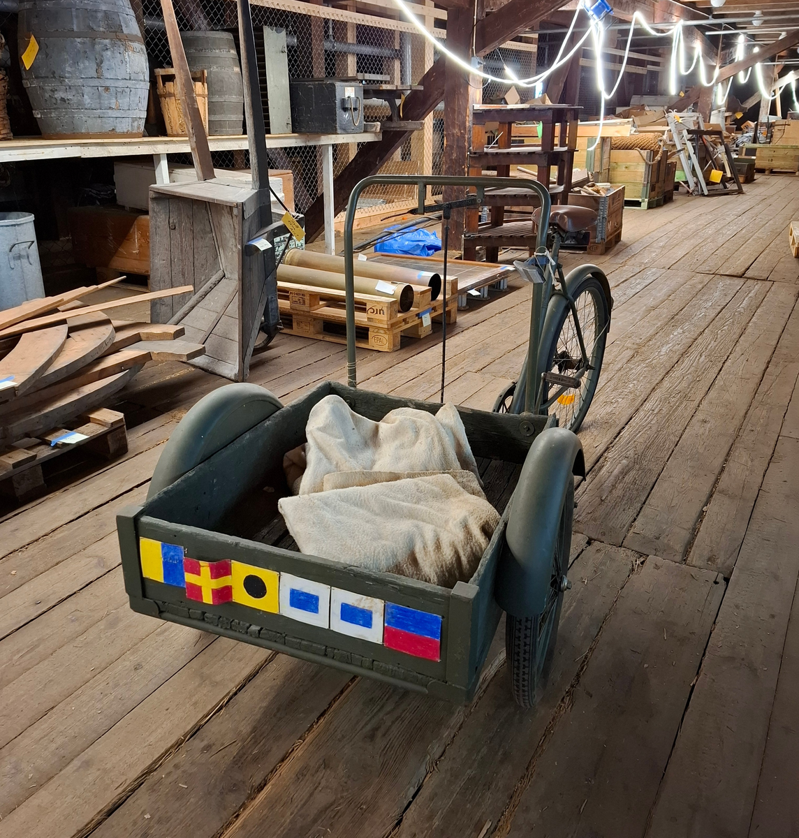 Militärgrön lådcykel av märke Monark med svarta hjul och brun lädersadel. Lådan är placerad i cykelns främre del och stabiliseras med två hjul. Styret består av en rektangulär ram monterad på lådans bakre del. Den bakre delen av cykeln ser ut som en helt vanlig cykel. 

I lådan ligger två tjocka vit-beige fleecefiltar. De båda filtarna är sydda som rektangulära påsar. I lådan finns också ett lås med texten "OPTIMUS ILCO", nyckel med texten "OPTIMUS" och kedja. 

På lådans framsida finns sex stycken handritade maritima singalflaggor på papper i olika utföranden som häftats på lådans främre del. Flaggorna ser ut att vara ritade med färgpennor/kritor. Flaggorna från vänster till höger-  
1. Gul och blå (Lodrätt):  Signalflagga K (Kilo) betyder: "Jag vill upprätta förbindelse med er".
2. Gult kryss mot röd bakgrund: Signalflagga R (Romeo) betyder: "Mitt fartyg gör ingen fart genom vattnet".
3. Gul med svart cirkel: Signalflagga I (India) betyder: "Jag ändrar min kurs babord hän".
4. Blå fyrkant mot vit bakgrund: Signalflagga S (Sierra) betyder: "Min maskin går back".
5. Blå fyrkant mot vit bakgrund: Signalflagga S (Sierra) betyder: "Min maskin går back"
6. Blå och röd (vågrätt): Signalflagga E (Echo) betyder: "Jag ändrar kurs styrbord hän".
Bokstäverna stavar tillsammans ordet "KRISSE".

Alla hjul lådcykeln behöver pumpas/lagas. Lådan i trä är också i någerlunda kritiskt skick.