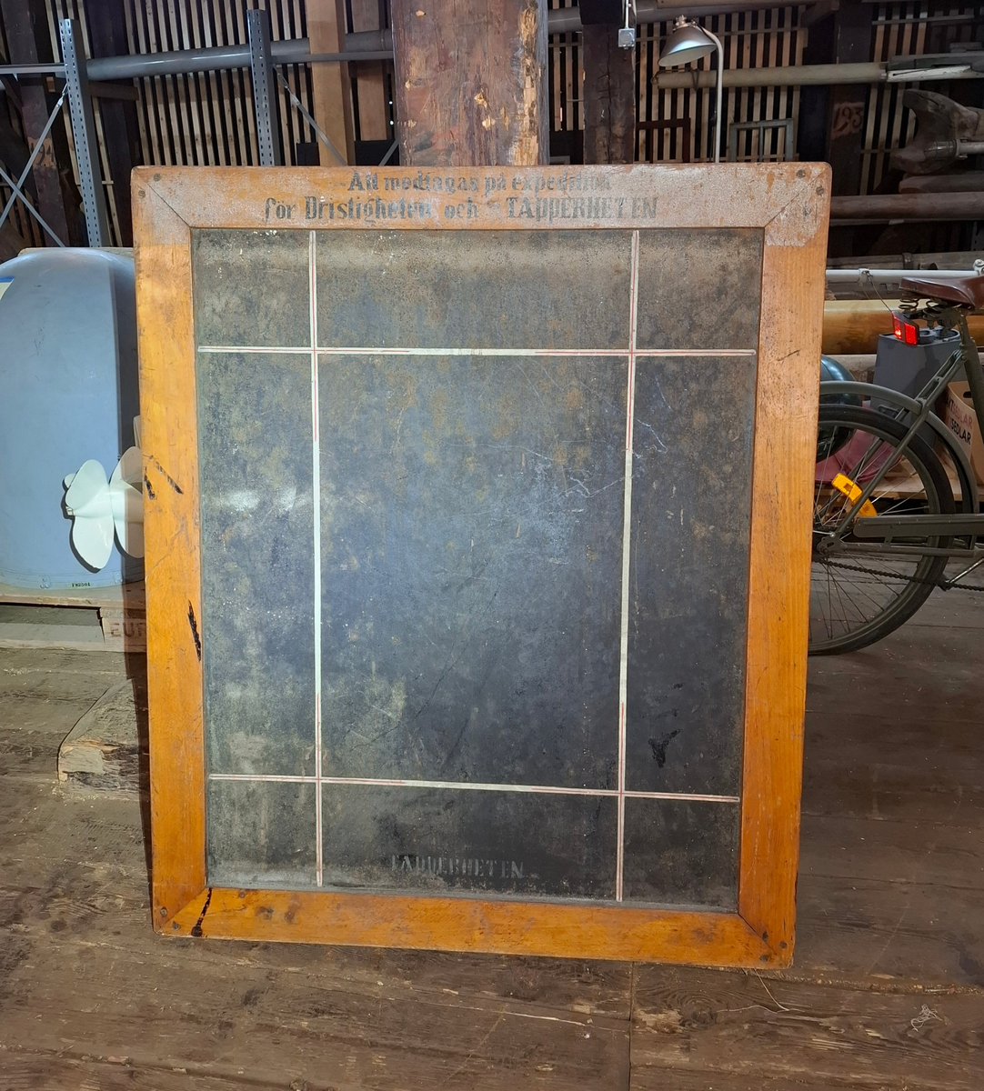 Griffeltavla för planering. Infattad i kraftig träram och sträv svart bakgrund. På tavlan finns vit- och röda streck i både vågrät och lodrätt riktning. På träramens övre del finns texten "Att medtagas på expedition för Dristigheten och TAPPERHETEN" i svart färg. På den nedre delen av tavlan står "TAPPEHETEN" i vit text mot den svarta bakgrunden. 

På tavlans baksidan finns en likadan svart 
tavelbakgrund med två treck i vit och röd färg placerade i ett kors.I lodrät rikning står texten "Dristigheten" i vit färg, placerad nedifrån och upp.