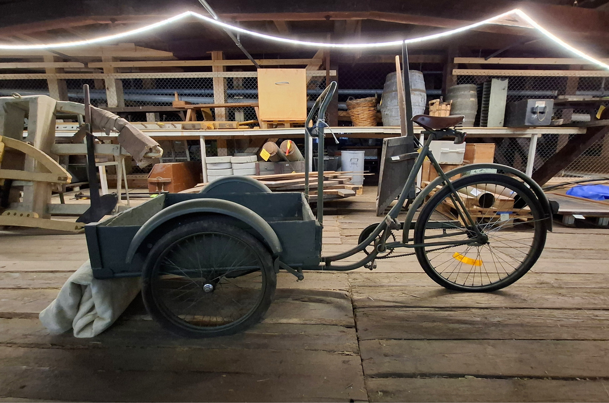 Militärgrön lådcykel av märke Monark med svarta hjul och brun lädersadel. Lådan är placerad i cykelns främre del och stabiliseras med två hjul. Styret består av en rektangulär ram monterad på lådans bakre del. Den bakre delen av cykeln ser ut som en helt vanlig cykel. 

I lådan ligger två tjocka vit-beige fleecefiltar. De båda filtarna är sydda som rektangulära påsar. I lådan finns också ett lås med texten "OPTIMUS ILCO", nyckel med texten "OPTIMUS" och kedja. 

På lådans framsida finns sex stycken handritade maritima singalflaggor på papper i olika utföranden som häftats på lådans främre del. Flaggorna ser ut att vara ritade med färgpennor/kritor. Flaggorna från vänster till höger-  
1. Gul och blå (Lodrätt):  Signalflagga K (Kilo) betyder: "Jag vill upprätta förbindelse med er".
2. Gult kryss mot röd bakgrund: Signalflagga R (Romeo) betyder: "Mitt fartyg gör ingen fart genom vattnet".
3. Gul med svart cirkel: Signalflagga I (India) betyder: "Jag ändrar min kurs babord hän".
4. Blå fyrkant mot vit bakgrund: Signalflagga S (Sierra) betyder: "Min maskin går back".
5. Blå fyrkant mot vit bakgrund: Signalflagga S (Sierra) betyder: "Min maskin går back"
6. Blå och röd (vågrätt): Signalflagga E (Echo) betyder: "Jag ändrar kurs styrbord hän".
Bokstäverna stavar tillsammans ordet "KRISSE".

Alla hjul lådcykeln behöver pumpas/lagas. Lådan i trä är också i någerlunda kritiskt skick.