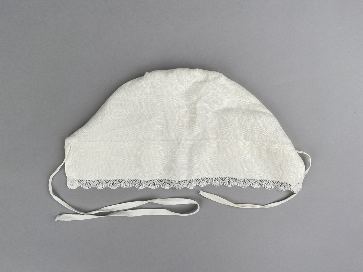 Hätta sk. fruhatt till Leksandsdräkten. Av vitt läskrus. Kantad längs framkanten med handknypplad spets. Snörning genom hål i nederkanten. Knyts ihop med bomullsband i nacken. Vitbroderi över sömmen bak.