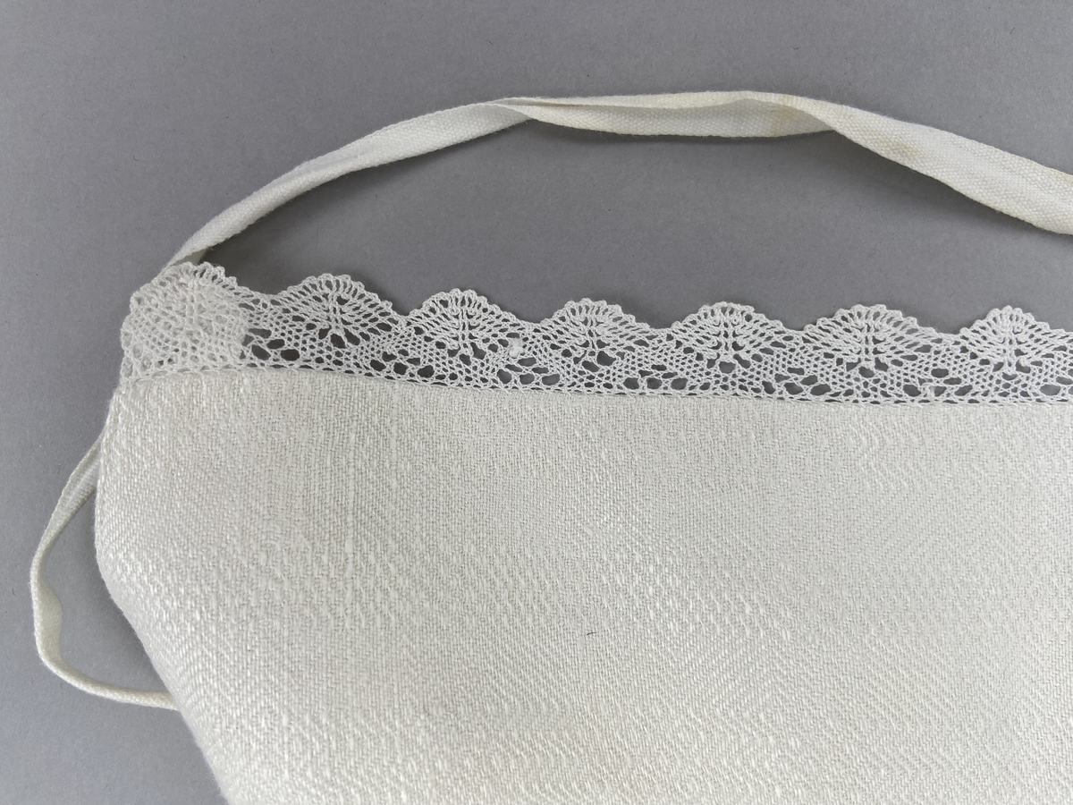 Hätta sk. fruhatt till Leksandsdräkten. Av vitt läskrus. Kantad längs framkanten med handknypplad spets. Snörning genom hål i nederkanten. Knyts ihop med bomullsband i nacken. Vitbroderi över sömmen bak.