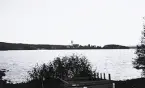 Bild över en sjö taget från en strandkant och med en kyrka och kust i bakgrunden. Text i album: 
