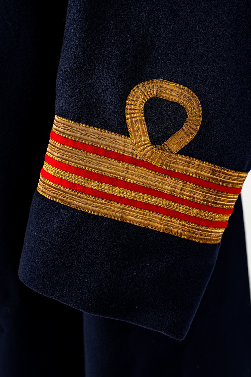 Kappa som hör till uniformen som användes av marinläkaren Anders Rudolf Prag.
Anders Prag kom tili Karlskrona 1929 som marinläkare, dispensärläkare och privatpraktiserande läkare, där hans största intresse alltid varit pediatriken, hans huvudintresse och specialitet. Anders Prag har här i staden gjort ett verkligt pionjärarbete i det att han startat barnavårdscentralsverksamheten, om vilken han aven hallit föreläsningar i Karlskrona läkareforening. I föreningen har han varit sekreterare och ordförande. Som marinläkare har Anders nått l:e marinläkargraden. De gåger han underhillit kollegerna med sång till luta, då hans sonora stamma klingat så vackert har varit verkliga högtidsstunder (ur Karlskrona Lakareförening 120 år Från hot om prygelstraff till fastställd arbetstid, SVEN SVENNERUD och HOLGER HOLMGREN 1978). "Gradbeteckningar med olikfärgat kläde mellan galonerna för civilmilitära tjänstemän med specialutbildning inom marinen; rött för marinläkare, vitt för marinintendent och lila för mariningenjör." S. 23 Flottans sjöofficersuniformer i Sjöhistoriska museets samlingar. Nils-Erik Melinder. Sida 38, samma skrift: "Från år 1937, utformades den för sjöofficeraren runda öglan till en rundad triangulär ögla, dessutom poängterad med olikfärgat kläde mellan galonerna. Statusen blev civilmilitär. Ett sammanhängande "öknamn" för den officerskategorin blev därför "päronklubben."