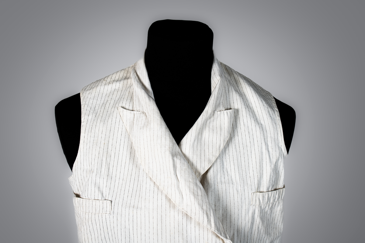 Väst som hör till uniformen som användes av marinläkaren Anders Rudolf Prag.
Anders Prag kom tili Karlskrona 1929 som marinläkare, dispensärläkare och privatpraktiserande läkare, där hans största intresse alltid varit pediatriken, hans huvudintresse och specialitet. Anders Prag har här i staden gjort ett verkligt pionjärarbete i det att han startat barnavårdscentralsverksamheten, om vilken han aven hallit föreläsningar i Karlskrona läkareforening. I föreningen har han varit sekreterare och ordförande. Som marinläkare har Anders nått l:e marinläkargraden. De gåger han underhillit kollegerna med sång till luta, då hans sonora stamma klingat så vackert har varit verkliga högtidsstunder (ur Karlskrona Lakareförening 120 år Från hot om prygelstraff till fastställd arbetstid, SVEN SVENNERUD och HOLGER HOLMGREN 1978). "Gradbeteckningar med olikfärgat kläde mellan galonerna för civilmilitära tjänstemän med specialutbildning inom marinen; rött för marinläkare, vitt för marinintendent och lila för mariningenjör." S. 23 Flottans sjöofficersuniformer i Sjöhistoriska museets samlingar. Nils-Erik Melinder. Sida 38, samma skrift: "Från år 1937, utformades den för sjöofficeraren runda öglan till en rundad triangulär ögla, dessutom poängterad med olikfärgat kläde mellan galonerna. Statusen blev civilmilitär. Ett sammanhängande "öknamn" för den officerskategorin blev därför "päronklubben."