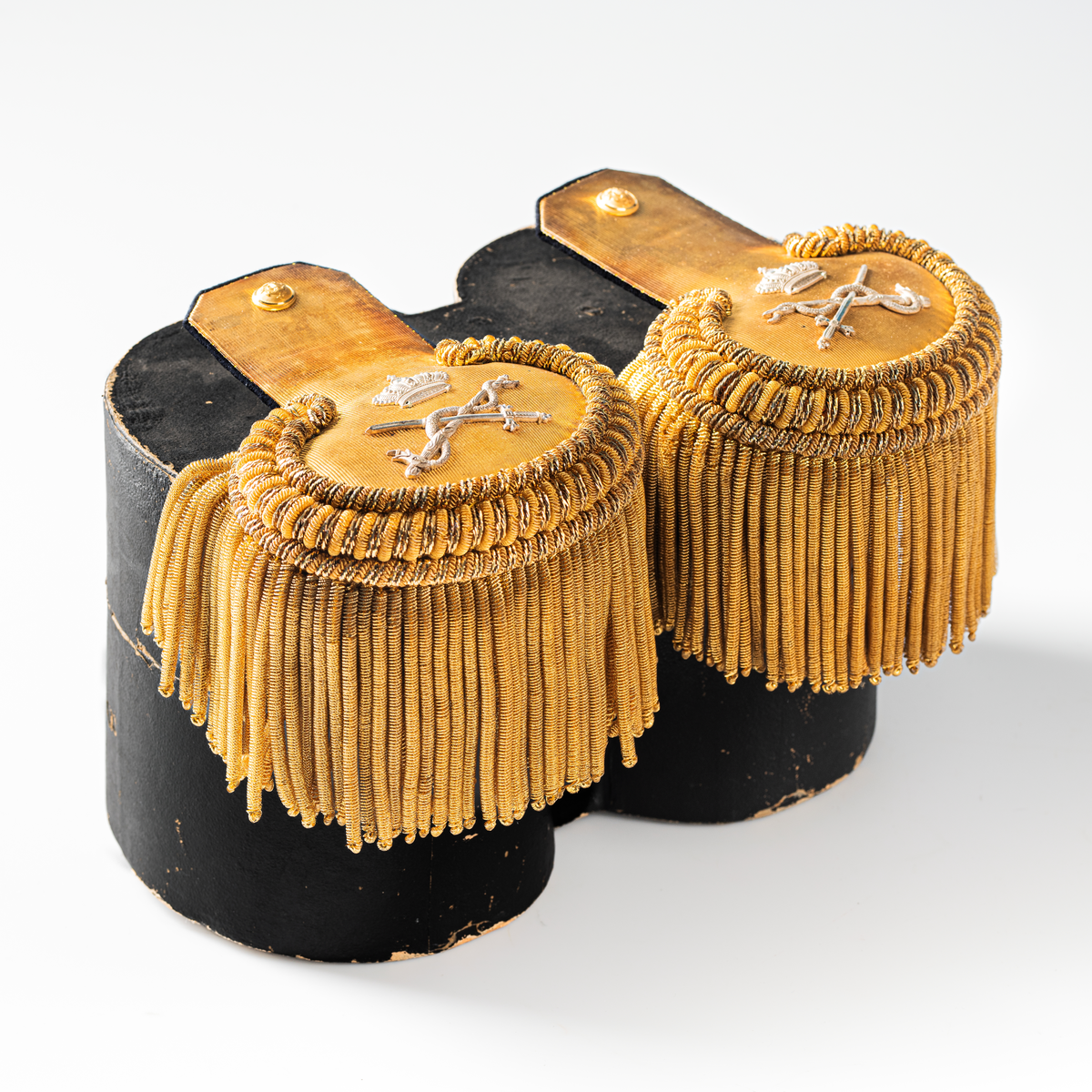 Ett par epåletter i ask av kartong som hör till uniformen som användes av marinläkaren Anders Rudolf Prag.
Anders Prag kom tili Karlskrona 1929 som marinläkare, dispensärläkare och privatpraktiserande läkare, där hans största intresse alltid varit pediatriken, hans huvudintresse och specialitet. Anders Prag har här i staden gjort ett verkligt pionjärarbete i det att han startat barnavårdscentralsverksamheten, om vilken han aven hallit föreläsningar i Karlskrona läkareforening. I föreningen har han varit sekreterare och ordförande. Som marinläkare har Anders nått l:e marinläkargraden. De gåger han underhillit kollegerna med sång till luta, då hans sonora stamma klingat så vackert har varit verkliga högtidsstunder (ur Karlskrona Lakareförening 120 år Från hot om prygelstraff till fastställd arbetstid, SVEN SVENNERUD och HOLGER HOLMGREN 1978). "Gradbeteckningar med olikfärgat kläde mellan galonerna för civilmilitära tjänstemän med specialutbildning inom marinen; rött för marinläkare, vitt för marinintendent och lila för mariningenjör." S. 23 Flottans sjöofficersuniformer i Sjöhistoriska museets samlingar. Nils-Erik Melinder. Sida 38, samma skrift: "Från år 1937, utformades den för sjöofficeraren runda öglan till en rundad triangulär ögla, dessutom poängterad med olikfärgat kläde mellan galonerna. Statusen blev civilmilitär. Ett sammanhängande "öknamn" för den officerskategorin blev därför "päronklubben."