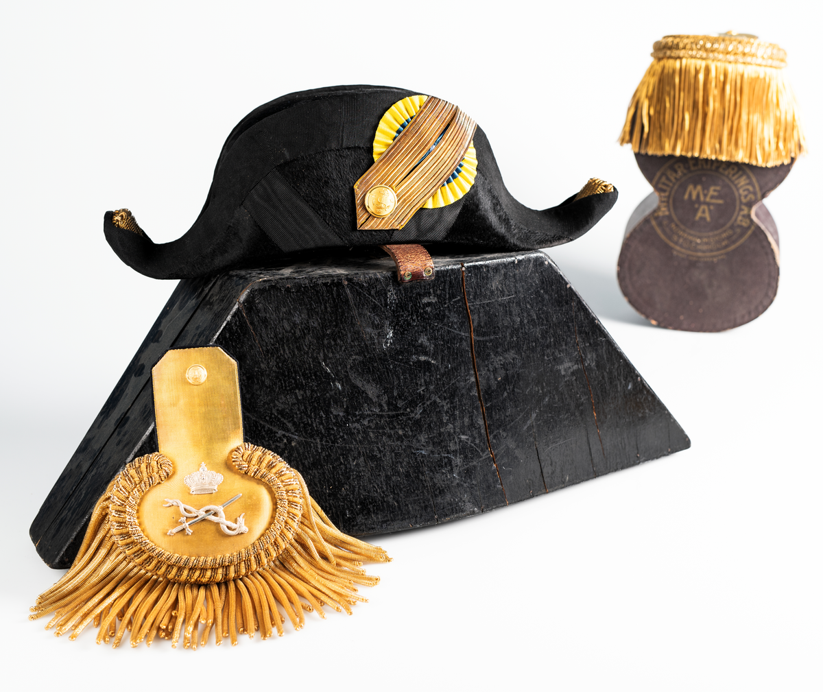 Ett par epåletter i ask av kartong som hör till uniformen som användes av marinläkaren Anders Rudolf Prag.
Anders Prag kom tili Karlskrona 1929 som marinläkare, dispensärläkare och privatpraktiserande läkare, där hans största intresse alltid varit pediatriken, hans huvudintresse och specialitet. Anders Prag har här i staden gjort ett verkligt pionjärarbete i det att han startat barnavårdscentralsverksamheten, om vilken han aven hallit föreläsningar i Karlskrona läkareforening. I föreningen har han varit sekreterare och ordförande. Som marinläkare har Anders nått l:e marinläkargraden. De gåger han underhillit kollegerna med sång till luta, då hans sonora stamma klingat så vackert har varit verkliga högtidsstunder (ur Karlskrona Lakareförening 120 år Från hot om prygelstraff till fastställd arbetstid, SVEN SVENNERUD och HOLGER HOLMGREN 1978). "Gradbeteckningar med olikfärgat kläde mellan galonerna för civilmilitära tjänstemän med specialutbildning inom marinen; rött för marinläkare, vitt för marinintendent och lila för mariningenjör." S. 23 Flottans sjöofficersuniformer i Sjöhistoriska museets samlingar. Nils-Erik Melinder. Sida 38, samma skrift: "Från år 1937, utformades den för sjöofficeraren runda öglan till en rundad triangulär ögla, dessutom poängterad med olikfärgat kläde mellan galonerna. Statusen blev civilmilitär. Ett sammanhängande "öknamn" för den officerskategorin blev därför "päronklubben."