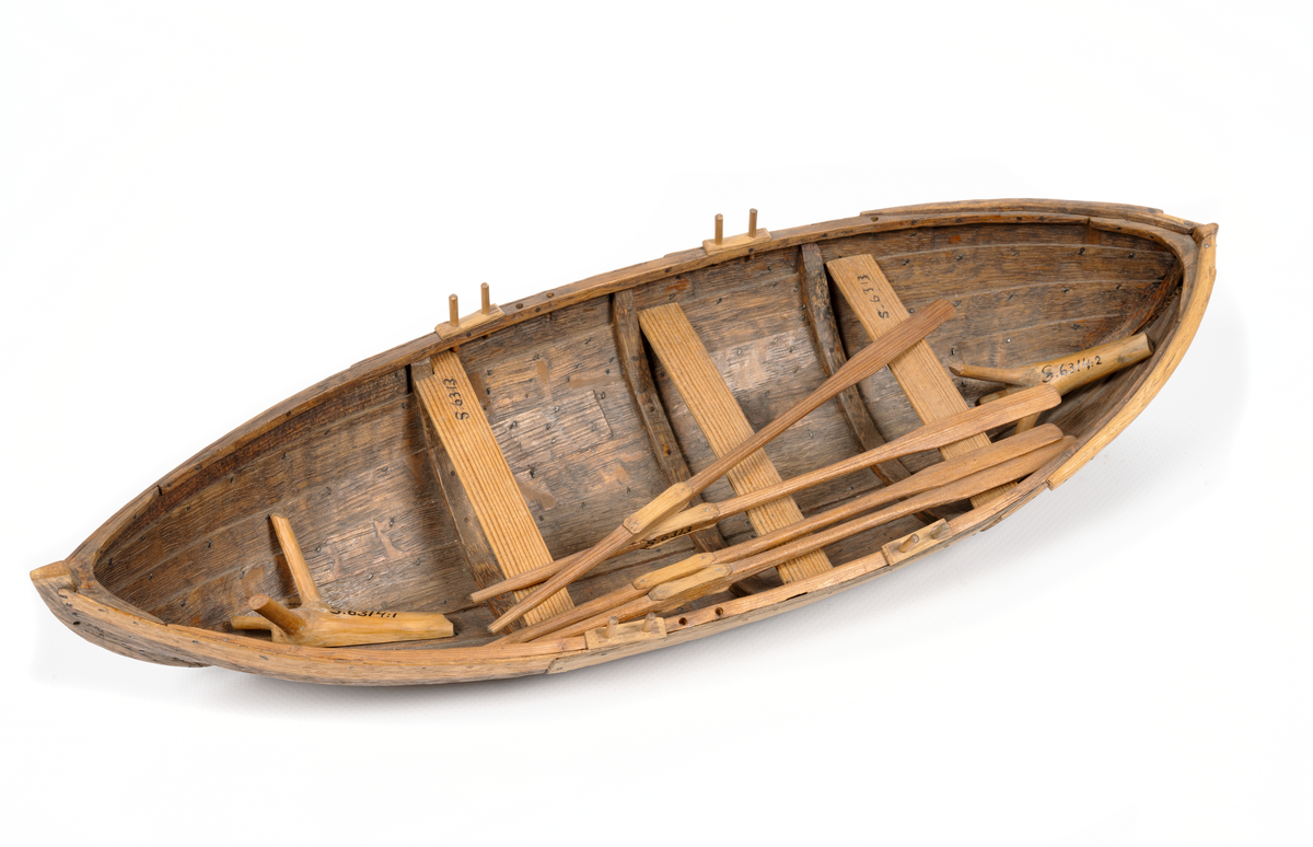 Båtmodell, rekonstruerad kopia av Kalmarfynd III, fullt utrustad. Bred kölplanka med stråkköl (ribba under) samt 4 bord på var sida, 3 spant, 4 årlägen för två roddare, 3 tofter, 4 åror.
