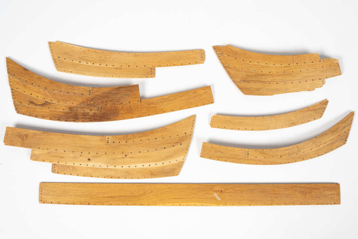 Fartygsmodell av ek, klinkbyggd på spant, högbordigt skepp (knarr)  ÄSKEKÄRRSBÅTEN  (fynd år 1933 fr. Göta älv, daterat 700 e. Kr.) Sidoroder på styrbordssidan, bordläggning förhöjd med ett bord i för- och akterskepp, liten back och halvdäck, kort kölsvin med mastspår.