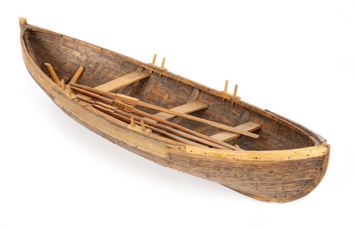 Båtmodell, rekonstruerad kopia av Kalmarfynd III, fullt utrustad. Bred kölplanka med stråkköl (ribba under) samt 4 bord på var sida, 3 spant, 4 årlägen för två roddare, 3 tofter, 4 åror.