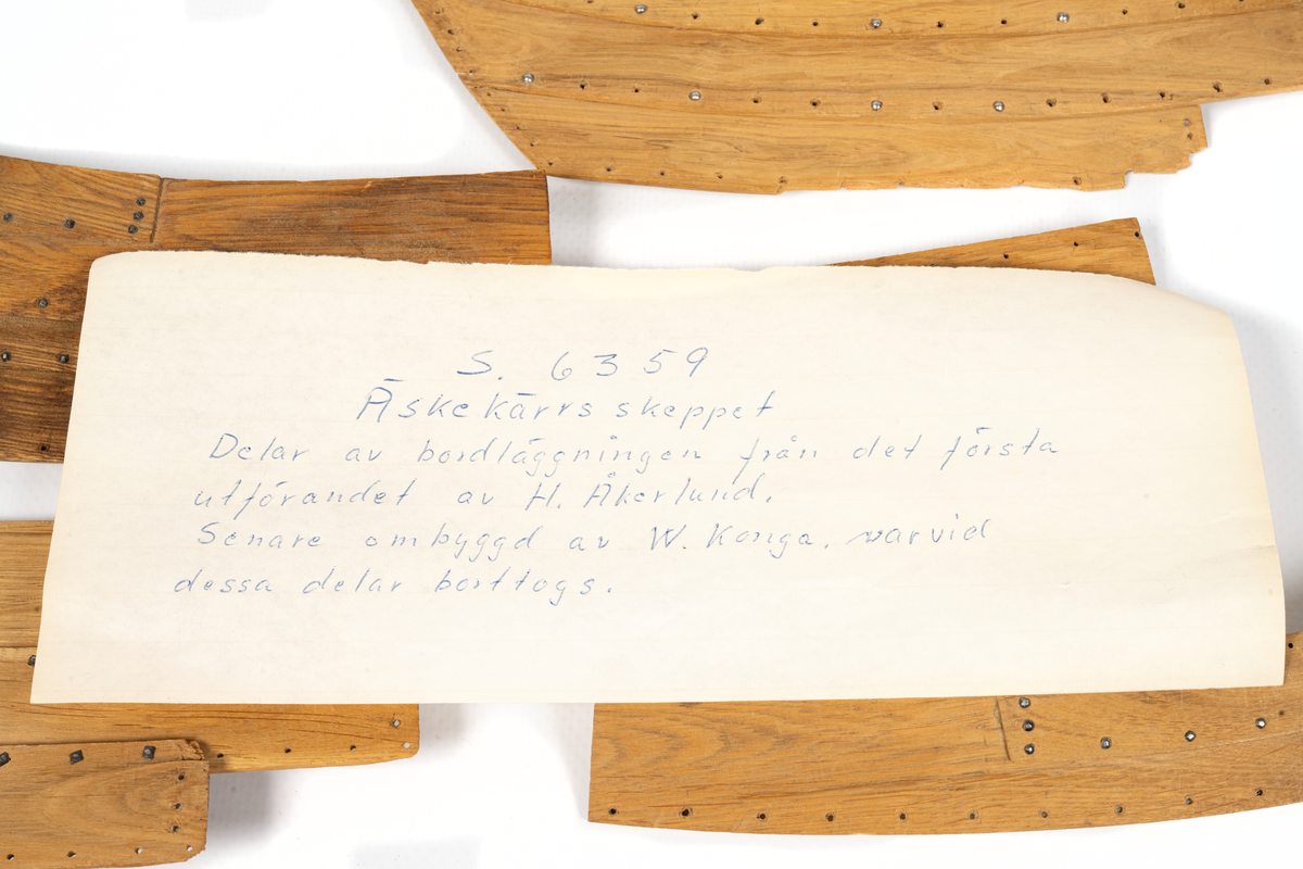 Fartygsmodell av ek, klinkbyggd på spant, högbordigt skepp (knarr)  ÄSKEKÄRRSBÅTEN  (fynd år 1933 fr. Göta älv, daterat 700 e. Kr.) Sidoroder på styrbordssidan, bordläggning förhöjd med ett bord i för- och akterskepp, liten back och halvdäck, kort kölsvin med mastspår.