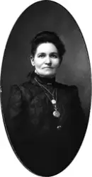 Portrett av en kvinne med mørkt hår og mørk, høyhalset overd