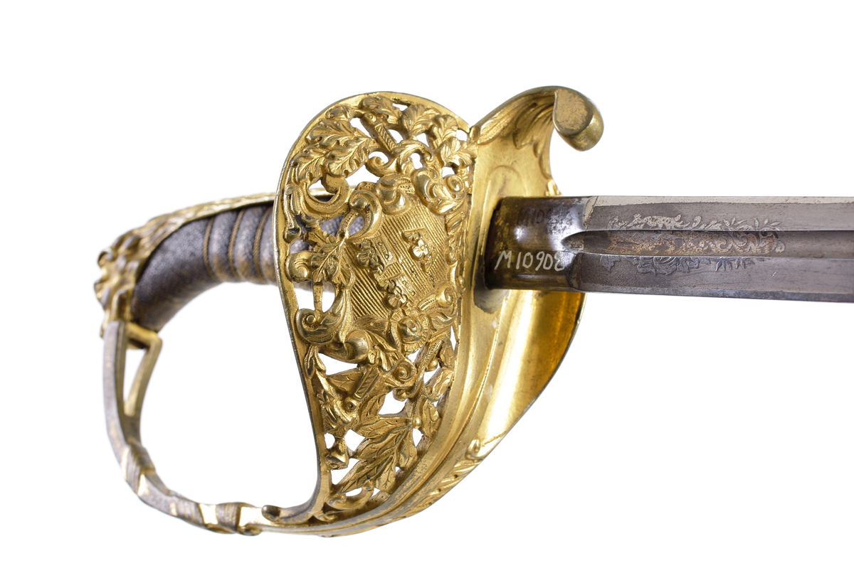 Officerssabel, möjligen modell M 1859 eller M 1899, med förgyllt mässingsfäste. Kaveln är klädd med svärtat fiskskinn, försedd med 8 räfflor lindade med snodd mässingstråd. Ryggbeslaget övergår i en kappa utförd som ett lejonhuvud. Parerplåten är enkelsidig och tillverkad av genombruten förgylld mässing. Klingan är tveeggad, försedd med blodskåror och etsade förgyllda ornament, Smålandsvapnet samt orden "Fäderneslandet" på ena sidan och "Konungen" på andra sidan.

Inskrivet i huvudbok år 1941.