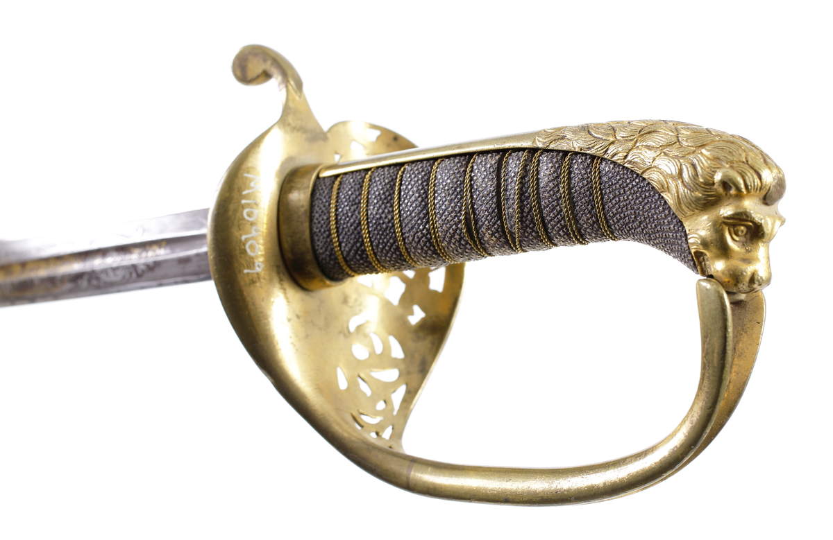 Officerssabel, M1899, med förgyllt mässingsfäste. Kaveln är klädd med svärtat fiskskinn, försedd med 8 räfflor lindade med snodd mässingstråd. Ryggbeslaget övergår i en kappa utformad som ett lejonhuvud. Parerplåten är tillverkad av gjuten mässing, enkelsidig med genombrutet kron- och bladmönster. Klingan är tveeggad, har blodrännor samt dekorationer av blomsterslingor, vapenemblem mm. På ena sidan står "Fäderneslandet" och på andra sidan "Konungen".
Baljan är tillverkad av svärtad plåt och har bygel. 

Inskriven i huvudbok år 1941.