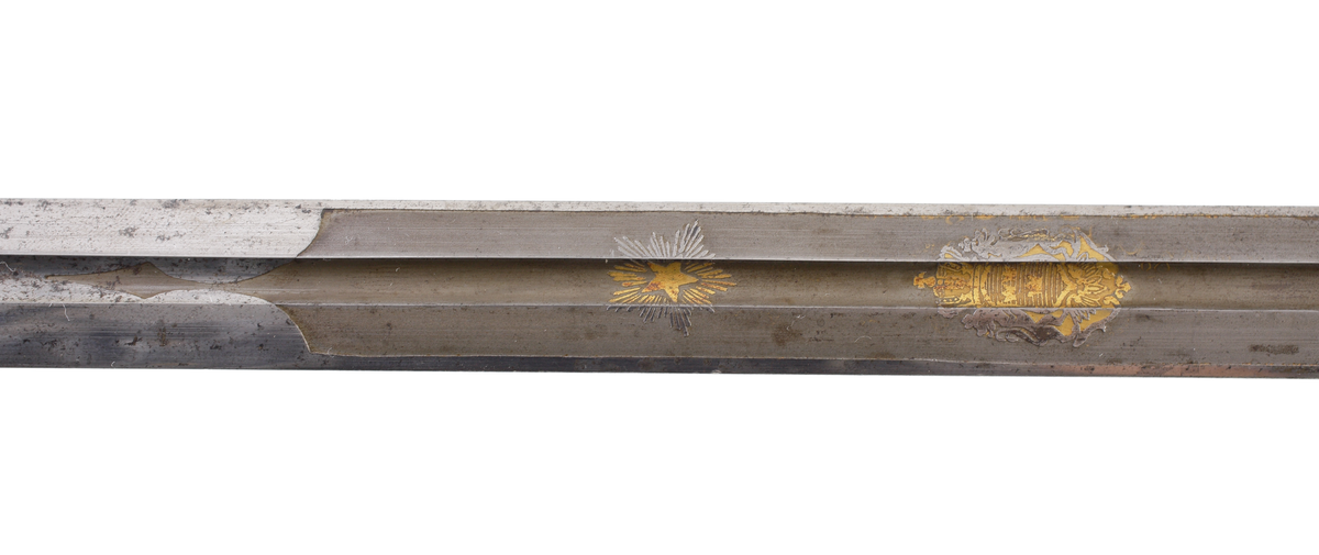 Officerssabel, M1899, med förgyllt mässingsfäste. Kaveln är klädd med svärtat fiskskinn, försedd med 8 räfflor lindade med snodd mässingstråd. Ryggbeslaget övergår i en kappa utformad som ett lejonhuvud. Parerplåten är tillverkad av gjuten mässing, enkelsidig med genombrutet kron- och bladmönster. Klingan är tveeggad, har blodrännor samt dekorationer av blomsterslingor, vapenemblem mm. På ena sidan står "Fäderneslandet" och på andra sidan "Konungen".
Baljan är tillverkad av svärtad plåt och har bygel. 

Inskriven i huvudbok år 1941.