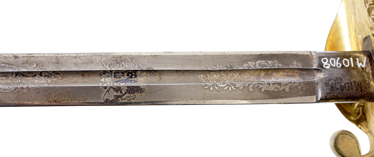 Officerssabel, möjligen modell M 1859 eller M 1899, med förgyllt mässingsfäste. Kaveln är klädd med svärtat fiskskinn, försedd med 8 räfflor lindade med snodd mässingstråd. Ryggbeslaget övergår i en kappa utförd som ett lejonhuvud. Parerplåten är enkelsidig och tillverkad av genombruten förgylld mässing. Klingan är tveeggad, försedd med blodskåror och etsade förgyllda ornament, Smålandsvapnet samt orden "Fäderneslandet" på ena sidan och "Konungen" på andra sidan.

Inskrivet i huvudbok år 1941.