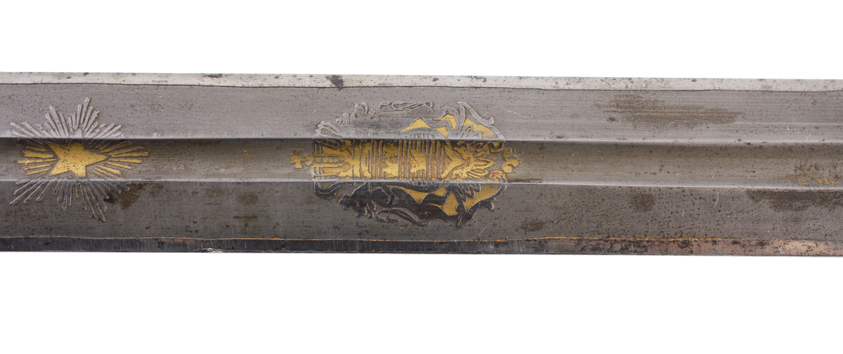 Officerssabel, M1899, med förgyllt mässingsfäste. Kaveln är klädd med svärtat fiskskinn, försedd med 8 räfflor lindade med snodd mässingstråd. Ryggbeslaget övergår i en kappa utformad som ett lejonhuvud. Parerplåten är tillverkad av gjuten mässing, enkelsidig med genombrutet kron- och bladmönster. Klingan är tveeggad, har blodrännor samt dekorationer av blomsterslingor, vapenemblem mm. På ena sidan står "Fäderneslandet" och på andra sidan "Konungen".
Baljan är tillverkad av svärtad plåt och har bygel. 

Inskriven i huvudbok år 1941.