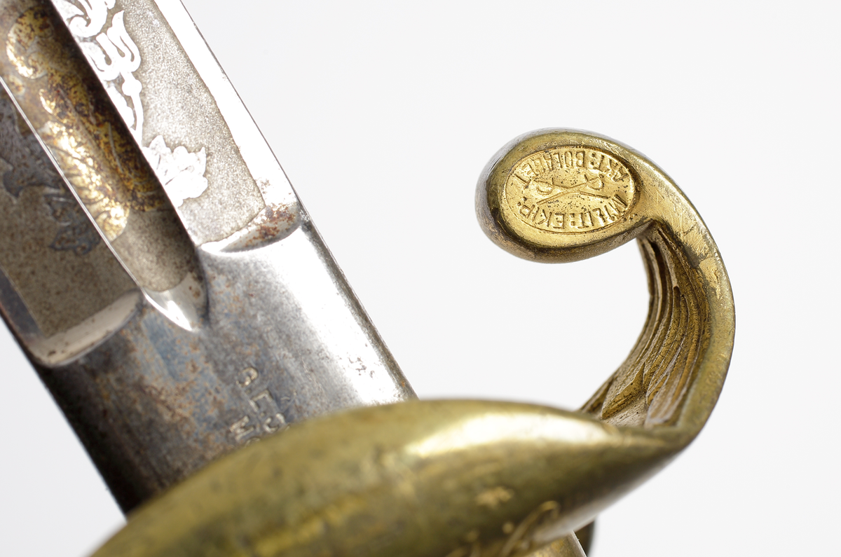 Officerssabel, möjligen modell M 1859 eller M 1899, med förgyllt mässingsfäste. Kaveln är klädd med svärtat fiskskinn, försedd med 8 räfflor lindade med snodd mässingstråd. Ryggbeslaget övergår i en kappa utförd som ett lejonhuvud. Parerplåten är enkelsidig och tillverkad av genombruten förgylld mässing. Klingan är tveeggad, försedd med blodskåror och etsade förgyllda ornament, Smålandsvapnet samt orden "Fäderneslandet" på ena sidan och "Konungen" på andra sidan.

Inskrivet i huvudbok år 1941.