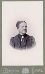 En medelålders okänd kvinna i mörk höghalsad blus med brosch