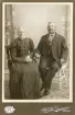 Ett äldre par poserar för fotografen. Mannen har en förtjänstmedalj med Oscar II:s bild i band runt halsen.
Helfigur. Ateljéfoto.