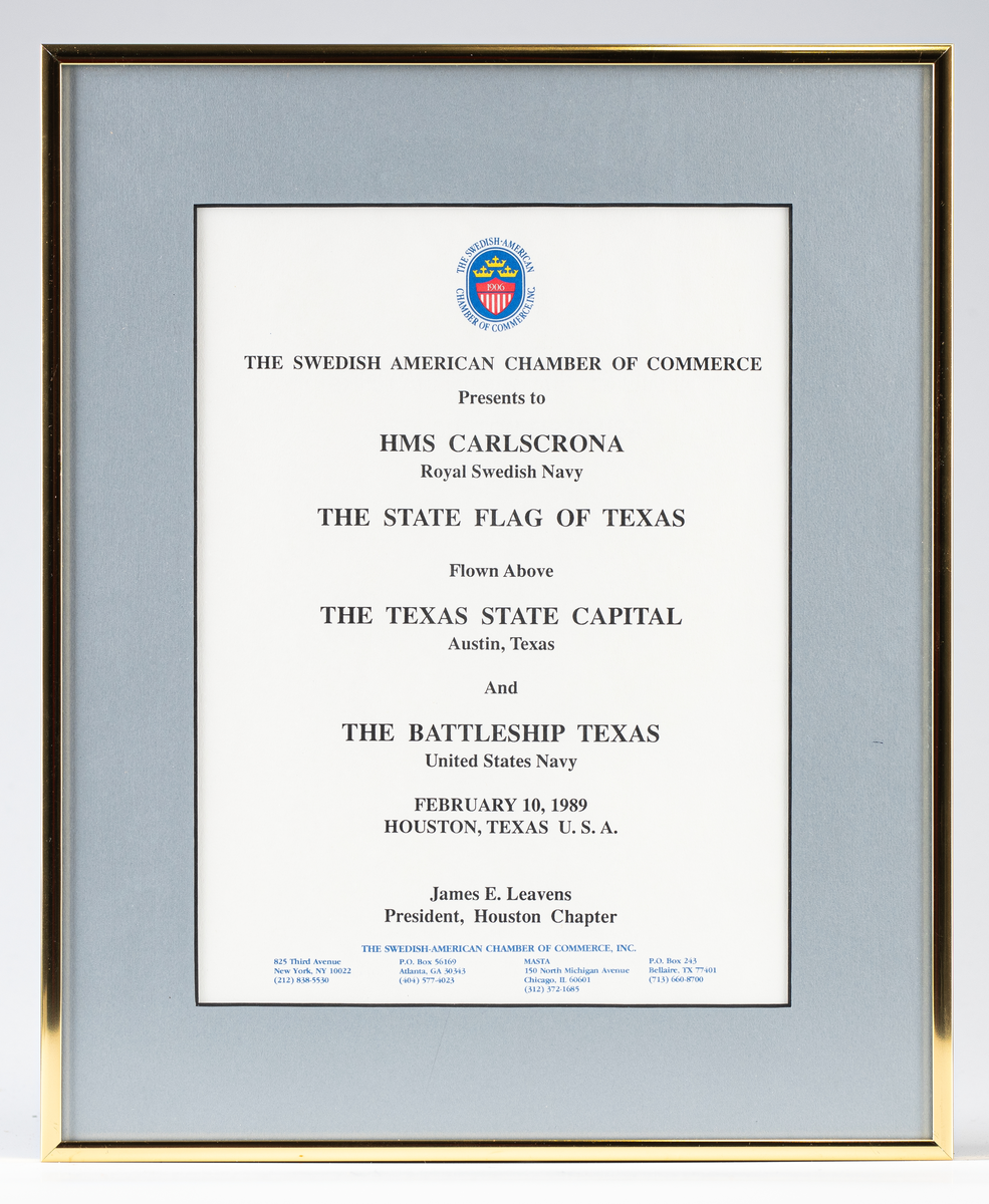Gåvobrev inom glas och ram från svensk-amerikanska handelskammaren för Texas statsflagga (MM18099). Överst emblem föreställande blå oval med tre gula kronor ovanför röd och vitrandig sköld försedd med årtalet 1906. Text i svart och blått. Grå bred passepartout 45 mm, ram av guldförgylld metall, 7 mm.
Neg.nr A309  1:15