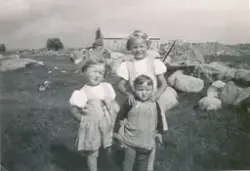 Tre små jenter på eit jorde. Steinur og løe i bakgrunnen.