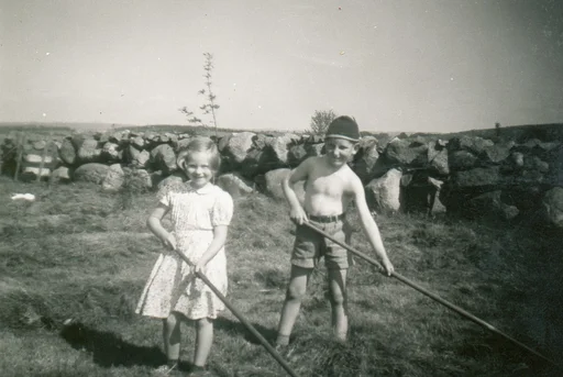 Ei lita jente og gut med lange river. Steingard i bakgrunnen.