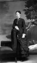 Helfigur studioportrett av en ung kvinne i mørk kjole som le