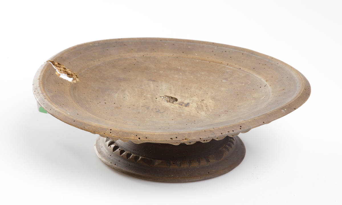 Kakfat av trä, på fot. Skuren dekor på fatets undersida och fot. Fatet är trasigt i ena kanten. Botten glödmärkt "R I. S.".
Inskrivet i huvudkatalog 1886-1887.