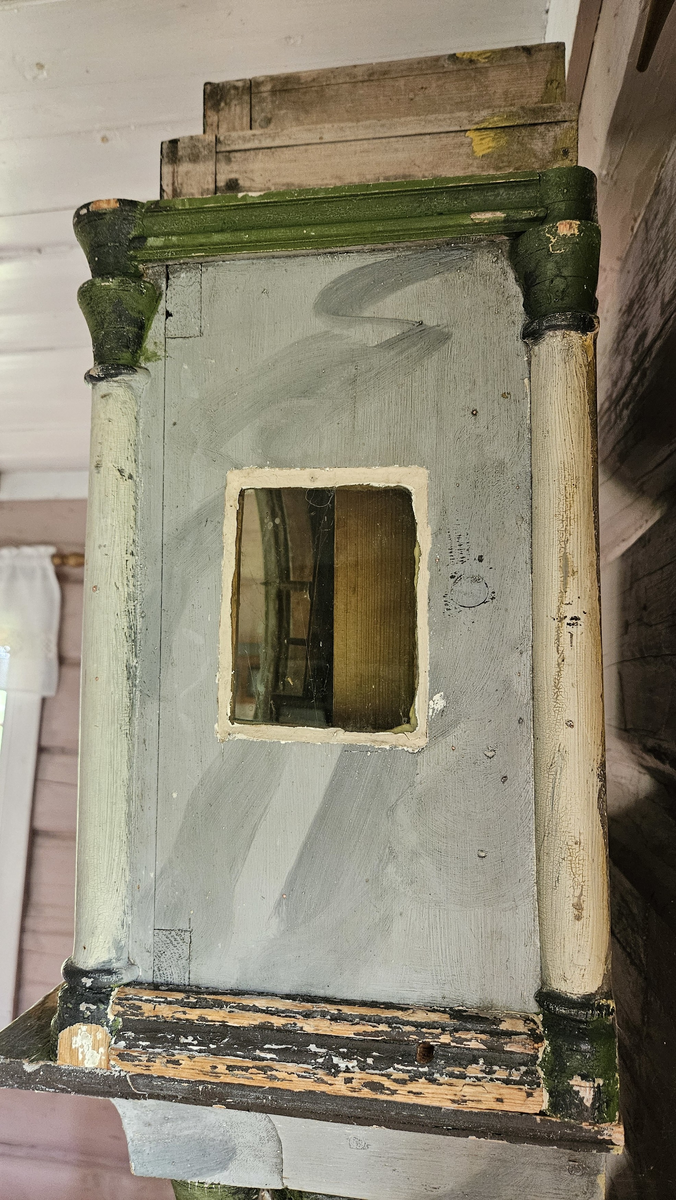 Kasse med dreide hjørnestolper og profilerte lister. Dør til lodd og pendel i midtfeltet. Vulstprofil. Glass på hver side av urverket. Grå marmorering, hvite og grønne og svarte kanter og lister. Foran tallskiva er det glassdør-sirkelformet, glasset mangler. Tallskive av tre, malt - svart romertall. På tallskiva rester av malte menneskefigurer i rødt, grønt, gult, blått. På toppen av kassa fem hull, formodentlig til å feste pyntekuler eller tilsvarende.