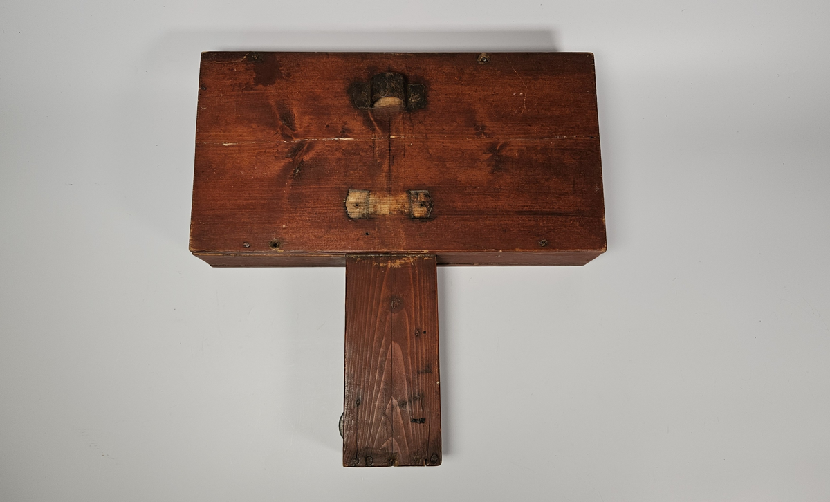 Nivelleringsinstrument bestående av trekasse med glassvindu for avlesing av mål. Fra skiva med mål henger et lodd. På baksida av trekassa er en bøyle; sannsynligvis for feste på et stativ.