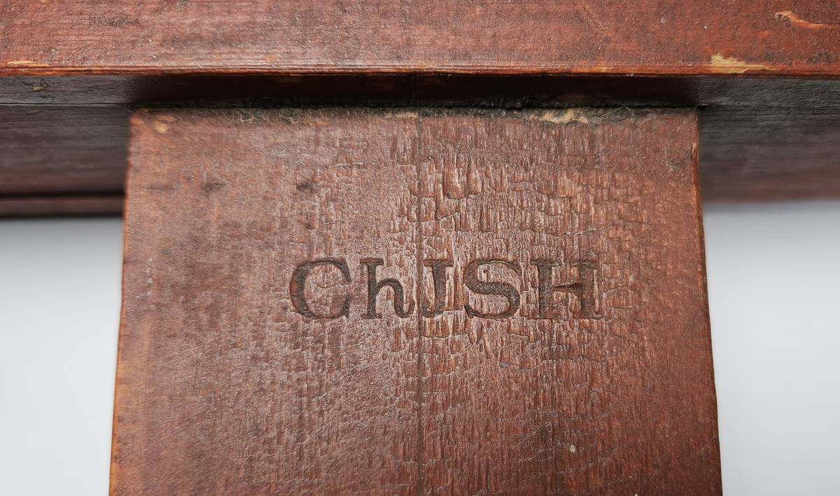 Nivelleringsinstrument bestående av trekasse med glassvindu for avlesing av mål. Fra skiva med mål henger et lodd. På baksida av trekassa er en bøyle; sannsynligvis for feste på et stativ.