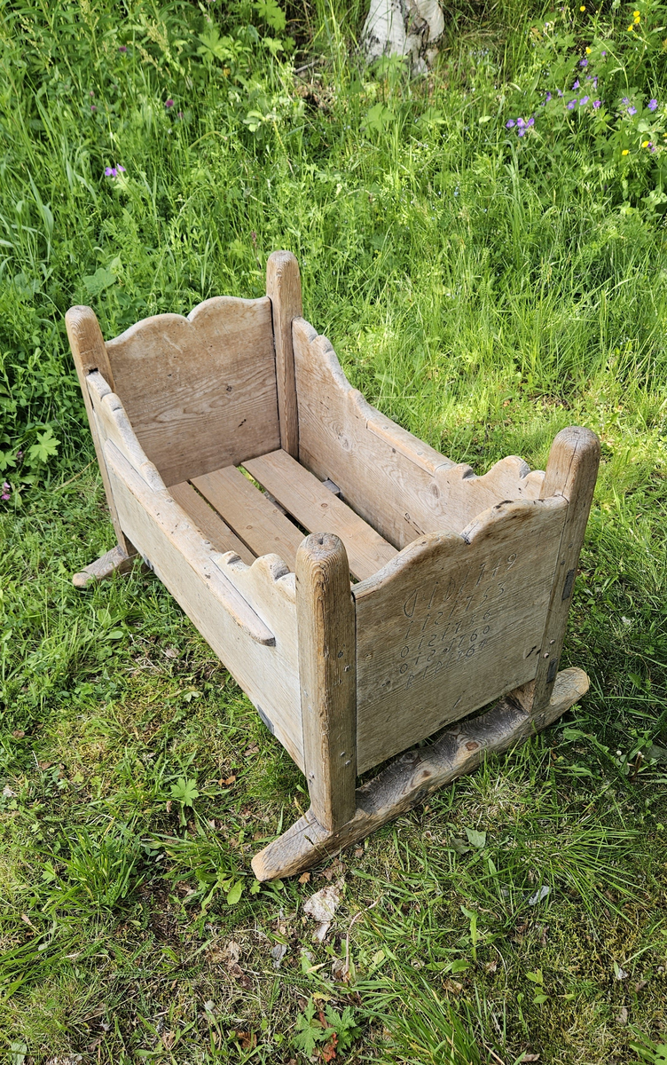 Gulvstående vugge med initialer og årstall skåret ut i hver kortende.