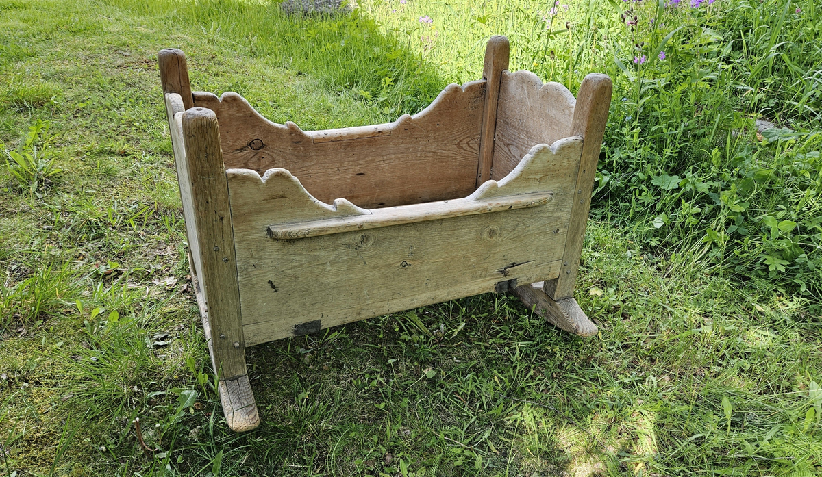 Gulvstående vugge med initialer og årstall skåret ut i hver kortende.