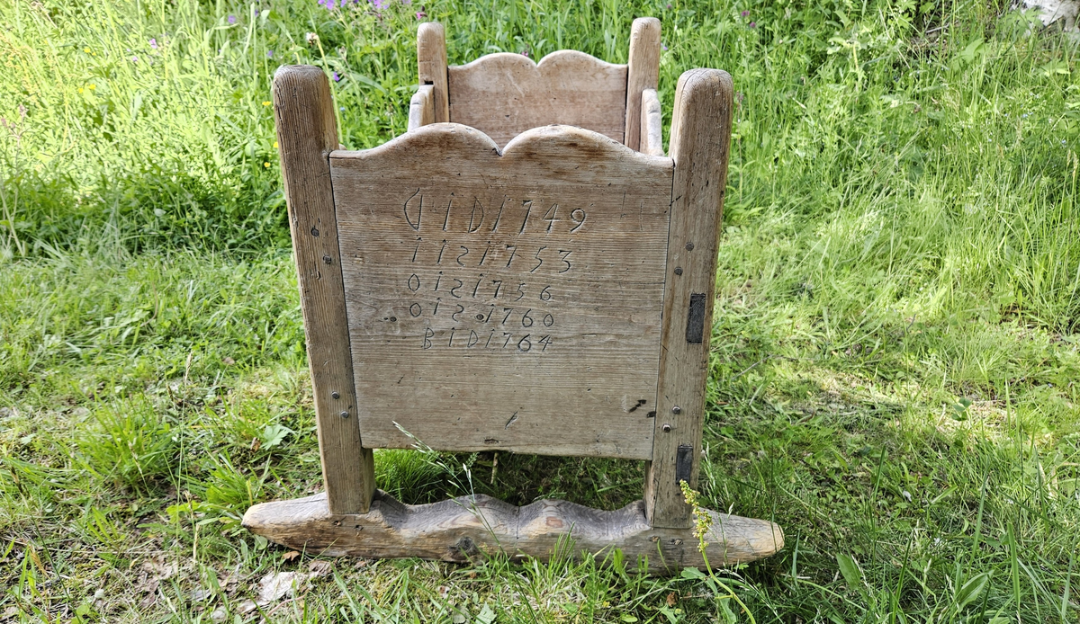 Gulvstående vugge med initialer og årstall skåret ut i hver kortende.