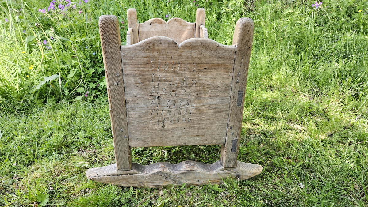 Gulvstående vugge med initialer og årstall skåret ut i hver kortende.