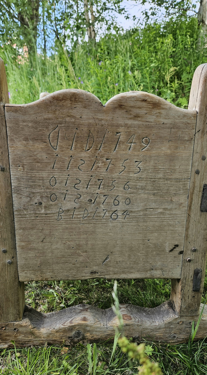 Gulvstående vugge med initialer og årstall skåret ut i hver kortende.