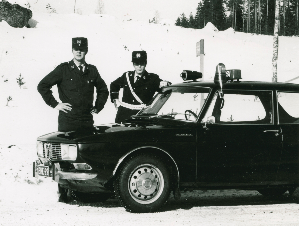 To uniformerte politifolk med politibil i vinterlandskap.