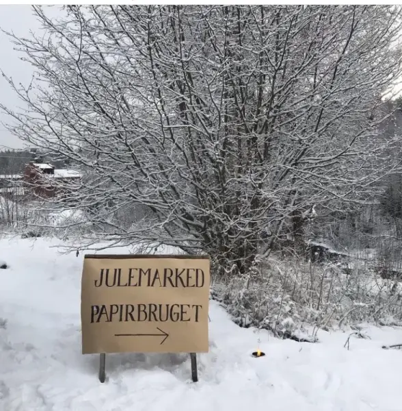 Snø på bakken og trærne, skilt med gråpapir som sier Julemarked Papirbruget