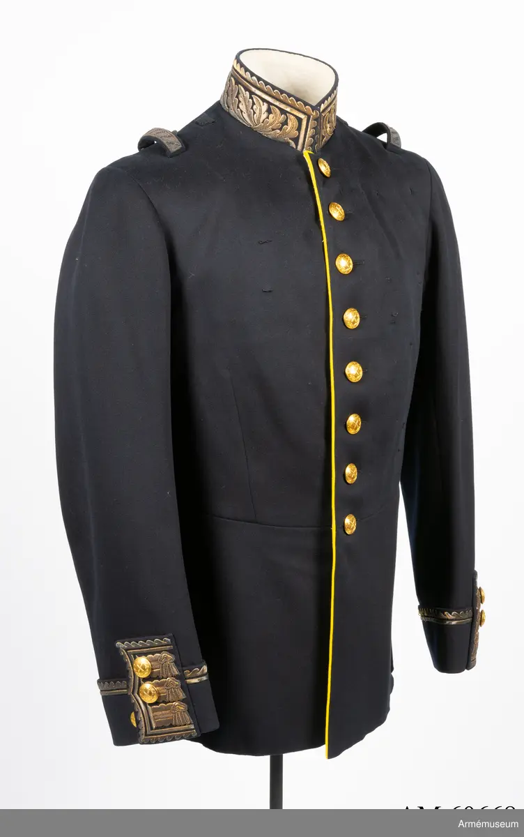 Vapenrock av mörkblått kläde med vitt foder i livet och gult foder i skörtet.
I innerfickan på vänster sida finns en etikett med text: ”G. U. HEURLIN & Cie 6/5 Stockholm 05 Öfverste Brändström”.