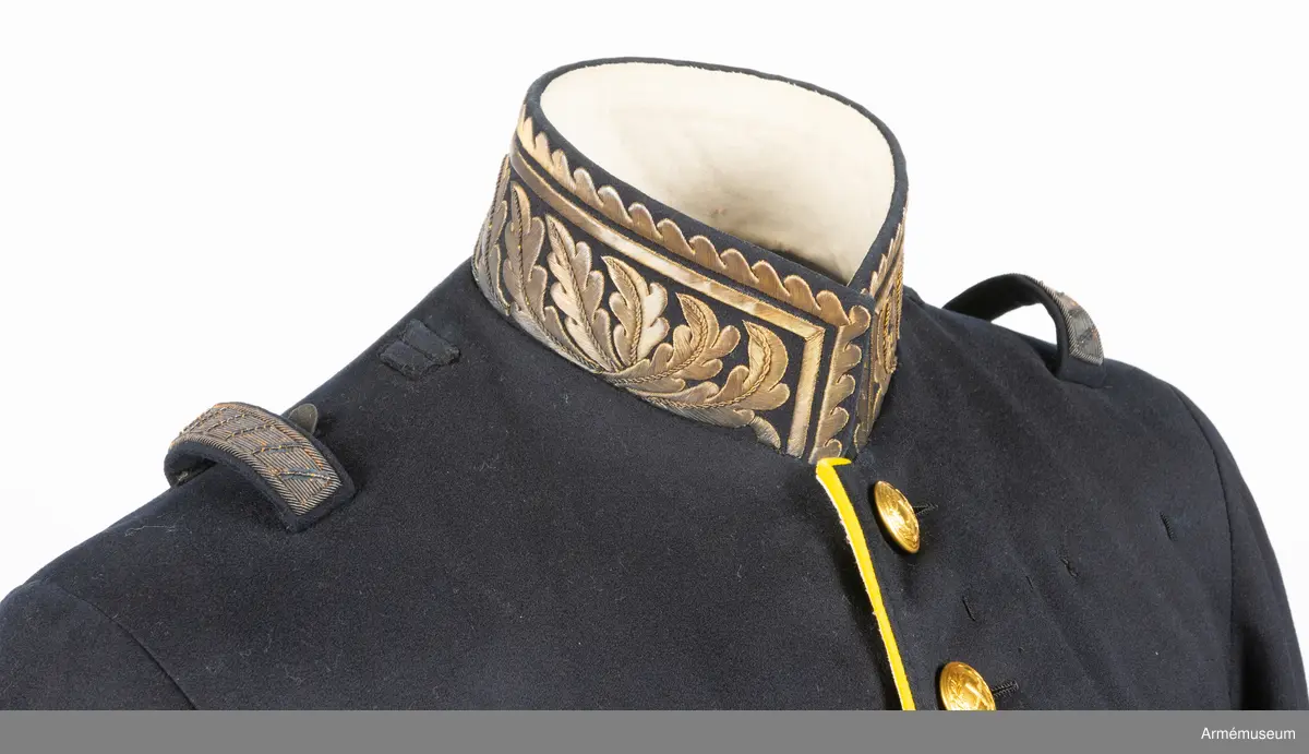 Vapenrock av mörkblått kläde med vitt foder i livet och gult foder i skörtet.
I innerfickan på vänster sida finns en etikett med text: ”G. U. HEURLIN & Cie 6/5 Stockholm 05 Öfverste Brändström”.