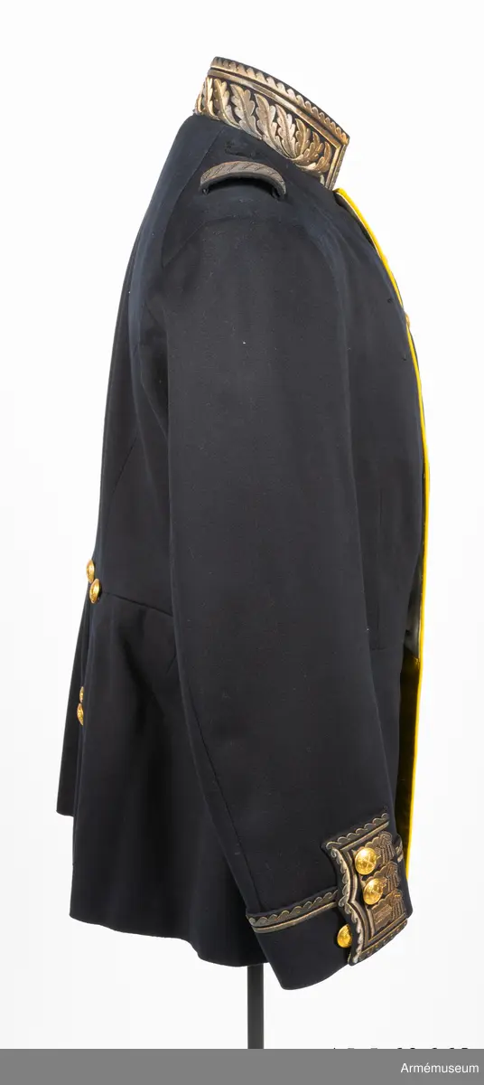 Vapenrock av mörkblått kläde med vitt foder i livet och gult foder i skörtet.
I innerfickan på vänster sida finns en etikett med text: ”G. U. HEURLIN & Cie 6/5 Stockholm 05 Öfverste Brändström”.